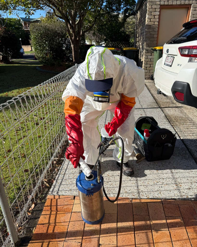 Pest technician in protective gear preparing a stainless steel sprayer on a residential driveway