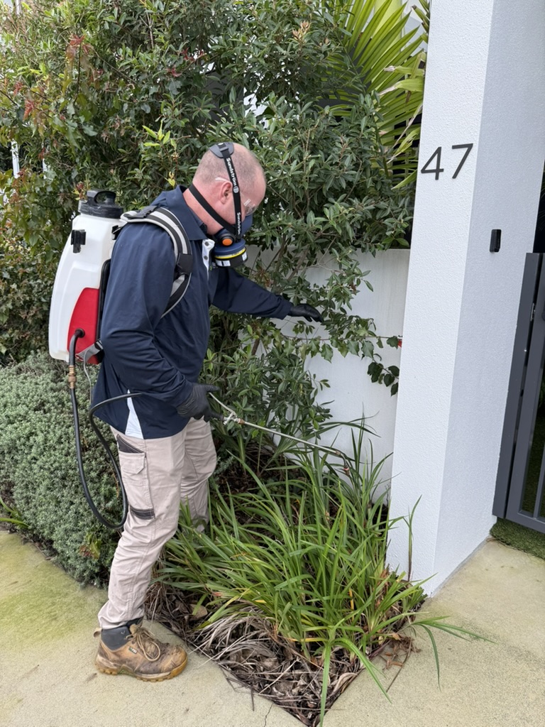 Pest control technician applying outdoor spray treatment during practical workplace training